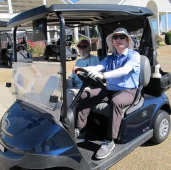 Two golfers in a cart, driver wearing a blue hat