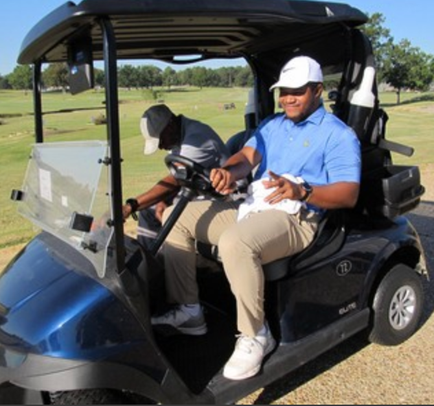 Two golfers in a cart, one in a blue shirt