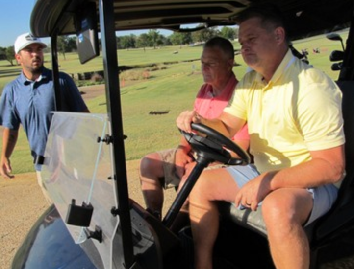 Three golfers near a cart, one in a yellow shirt