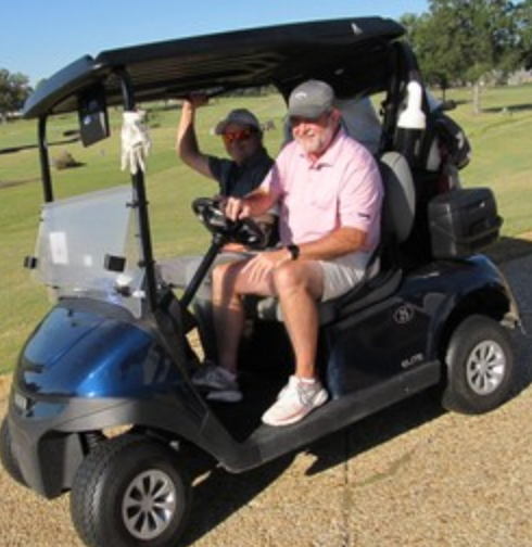 Two golfers in a cart, one in a pink shirt