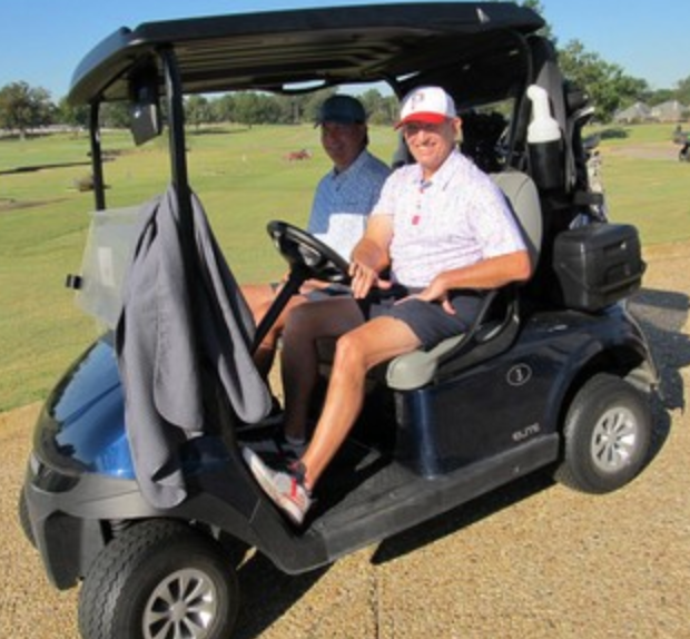 Two golfers in a cart, one wearing a red cap