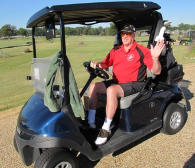 Golfer in a red shirt waving from a golf cart