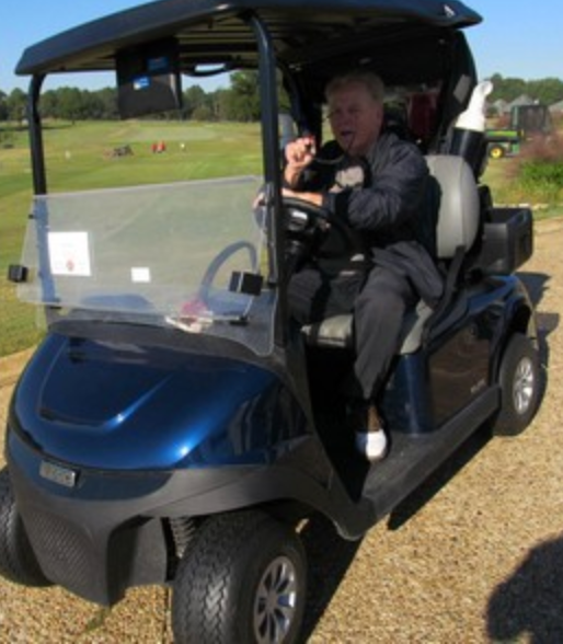 Golfer in a dark jacket riding solo in a golf cart