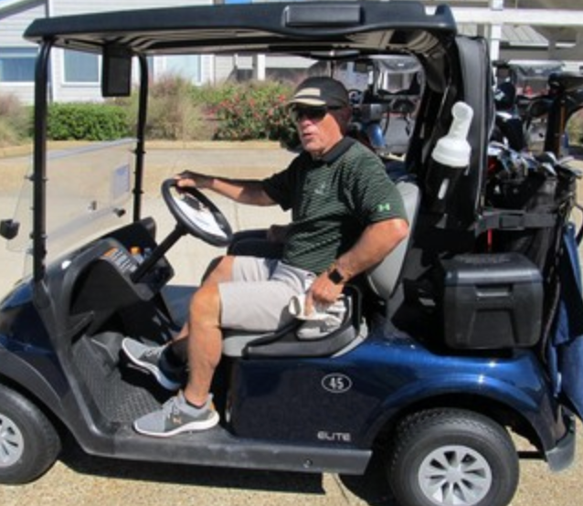 Golfer in a green shirt driving a golf cart solo