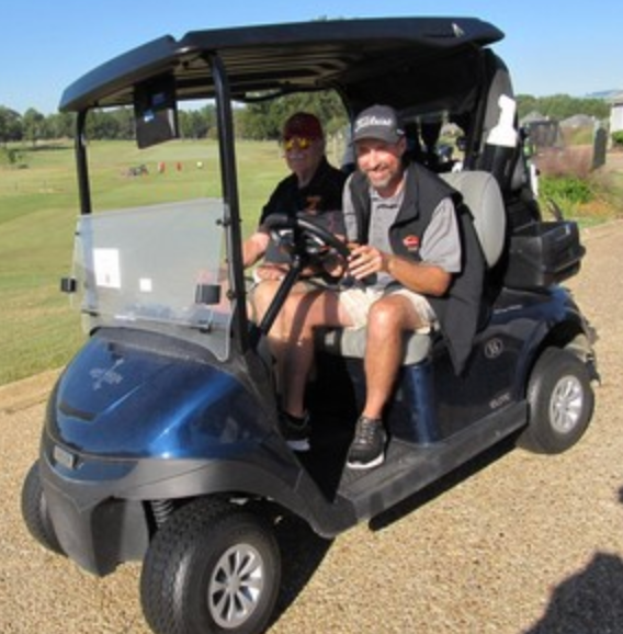 Two golfers in a cart, driver wearing a Titleist vest
