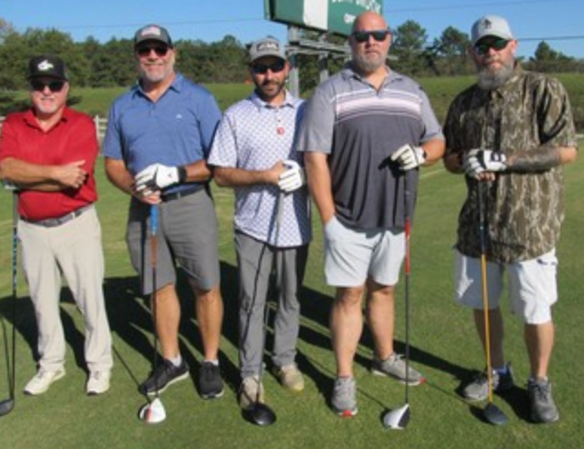Five golfers lined up at the tee box
