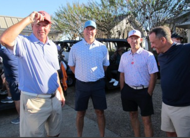 Four golfers posing together near golf carts