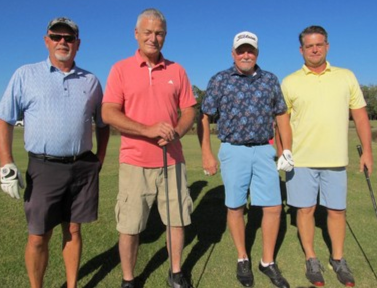 Foursome posing on the course, one in a coral shirt