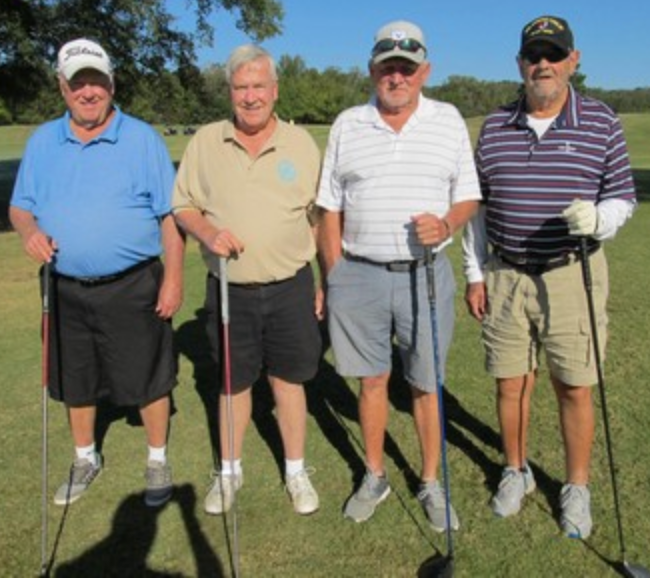 Foursome posing on the course, one in a striped shirt
