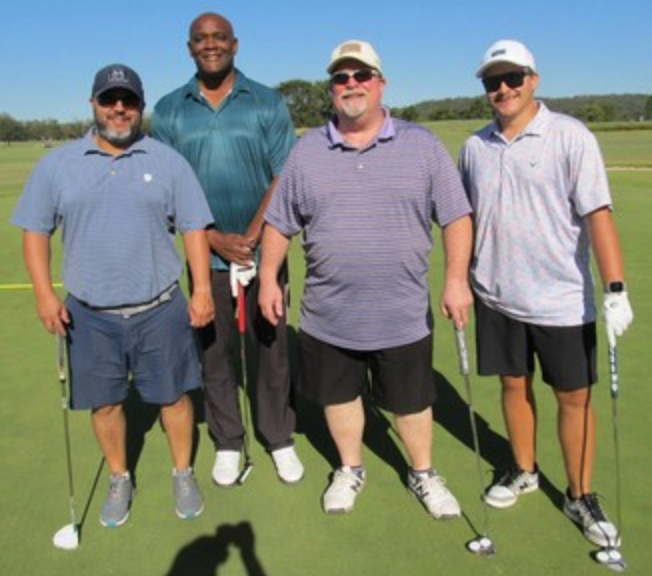 Foursome posing on the course, one in a Titleist cap
