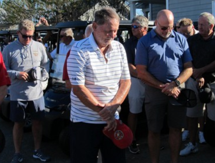 Golfers bowing heads in prayer before tournament
