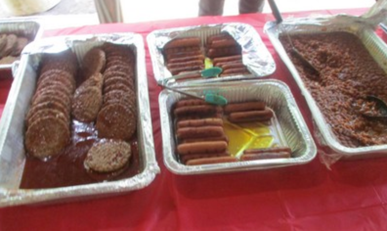 Hamburgers and hot dogs in foil trays on red table