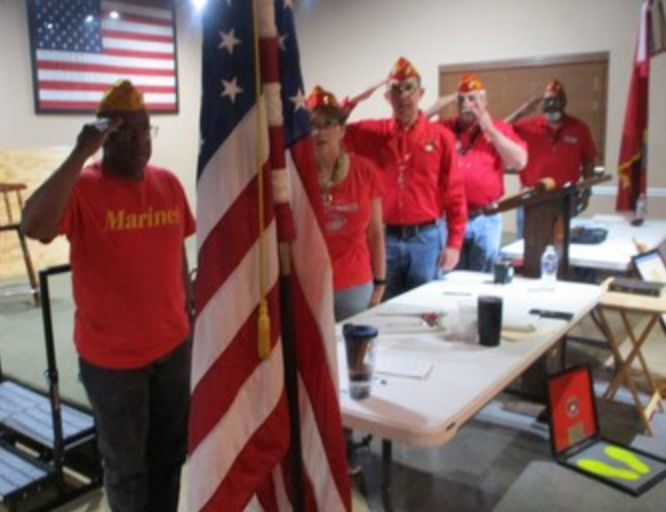 Members saluting the American flag at indoor meeting