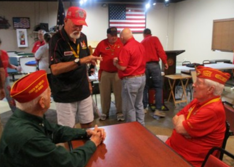 Members in red caps conversing at table with flags in background
