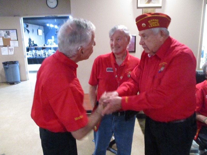 Three veterans in red uniforms conversing indoors