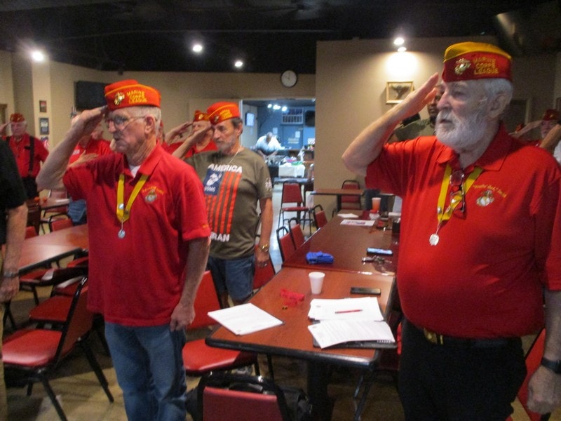 Veterans in red shirts saluting indoors